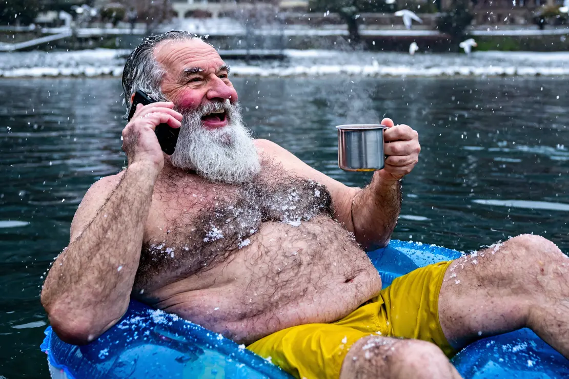 Alter Mann telefoniert auf Schwimmring sitzend im winterlichen See.